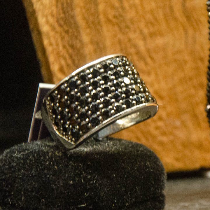 Wide silver band set with small black stones on a black stand