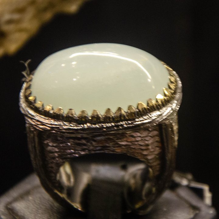 Large pale cabochon ring in textured silver on a black stand