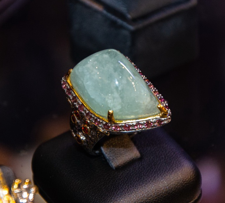 Ring with a large pale blue-green cabochon framed by a row of small red stones