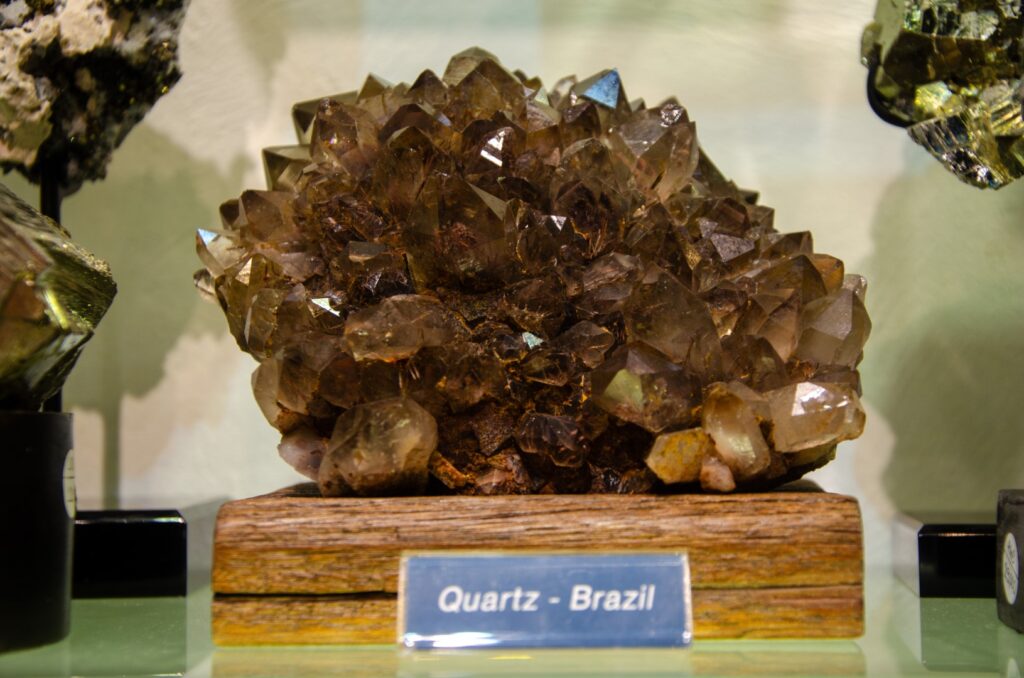 Brown quartz cluster on a wooden base, labeled Quartz Brazil